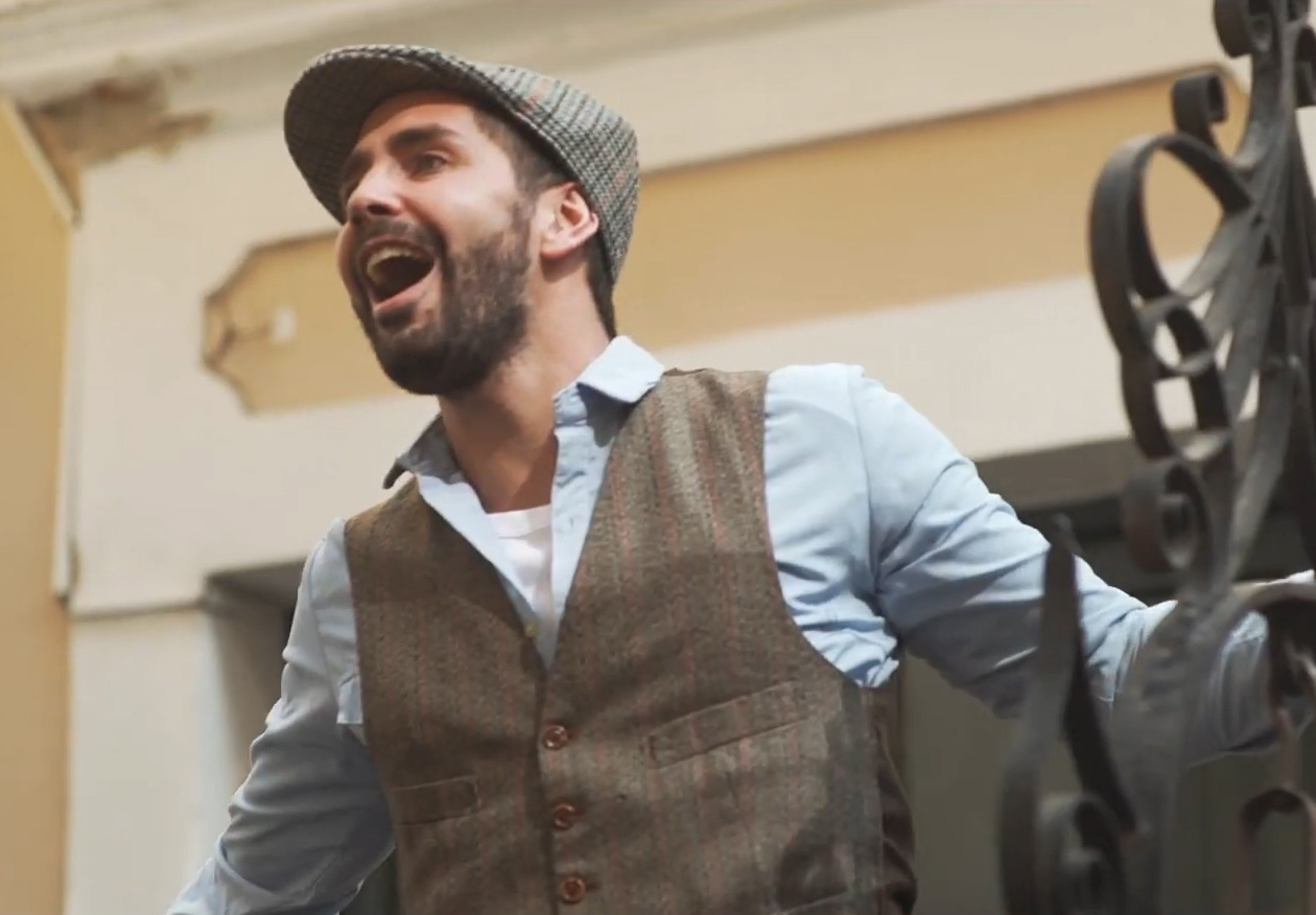 Home Frame de una obra audiovisual: un personaje canta desde una escalera.